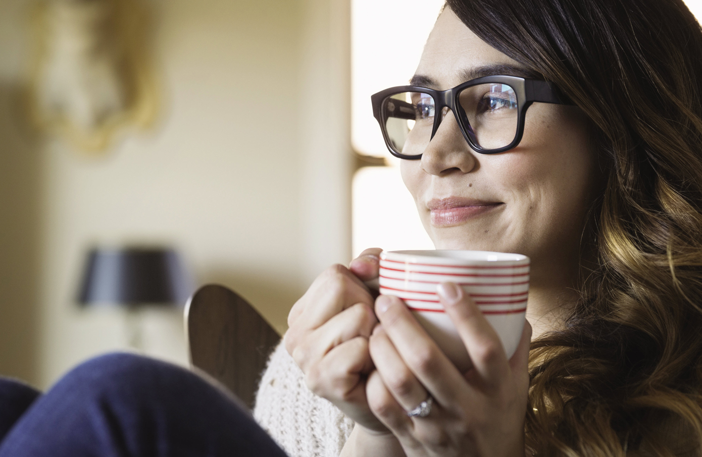 A woman in glasses drinks holds a coffee mug.
