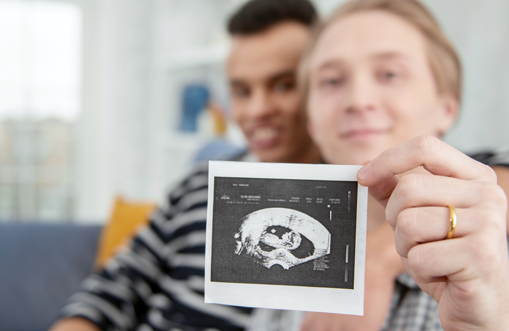 A same-sex couple hold up an ultrasound photo.