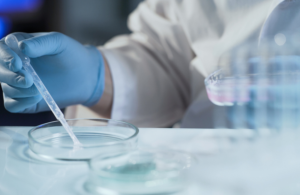 A healthcare professional uses a dropper and petri dish.