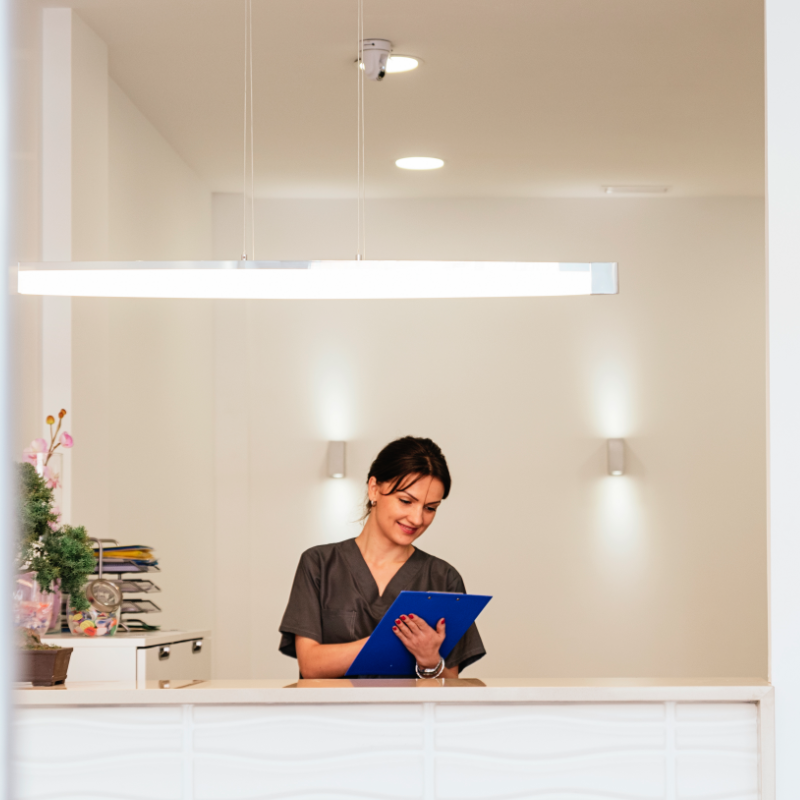 medical professional standing behind desk in reception looking at tablet