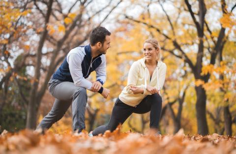 A couple do lunges together outdoors in autumn.